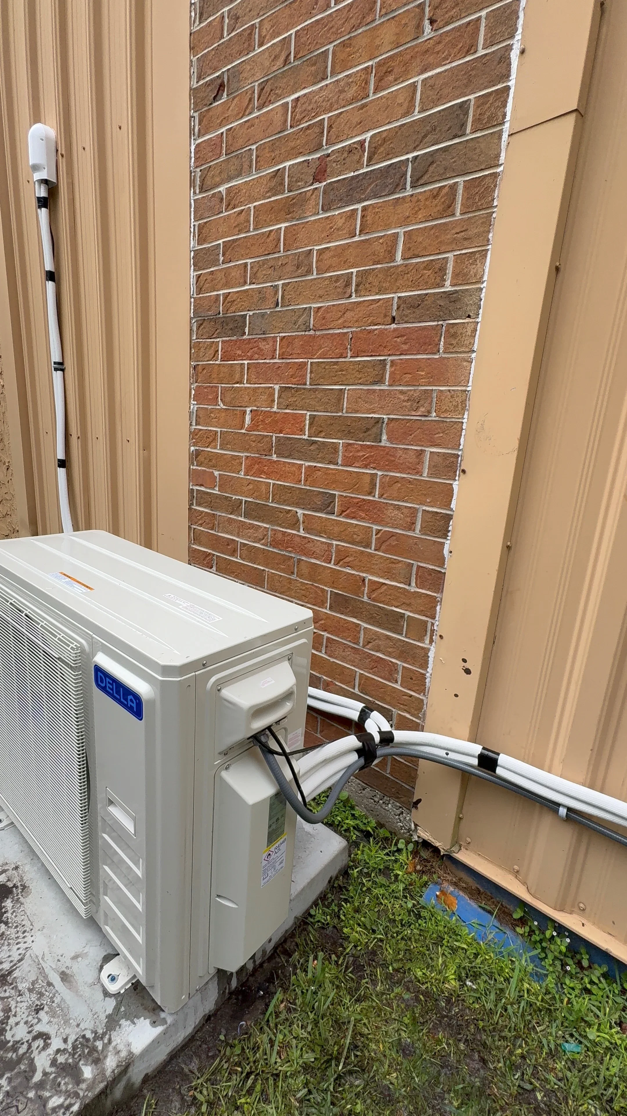 White mini-split heat pump condenser unit installed on brick wall with refrigerant lines